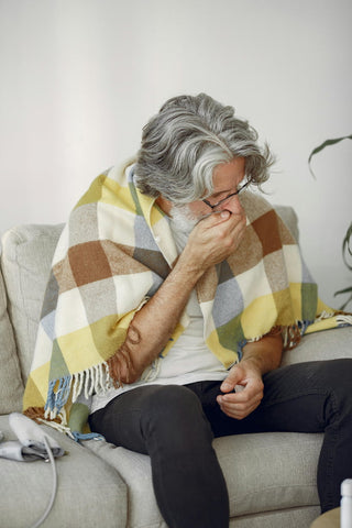 Un homme plus âgé toussant dans sa main avec une couverture sur lui