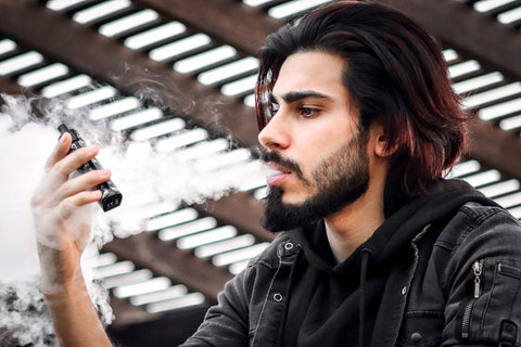 Un homme fumant un stylo vape et soufflant de la fumée