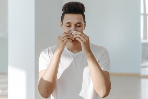 A man blowing his nose in a white room