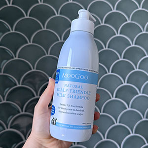 hand holding bottle of shampoo in front of tiled bathroom wall