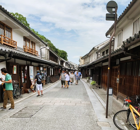 A busy street in a classic Japanese town with wooden structures, pedestrians and clear skies
