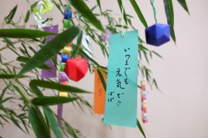 Teal coloured tanabata card decoration hanging from a bamboo tree with Japanese calligraphy written on top.