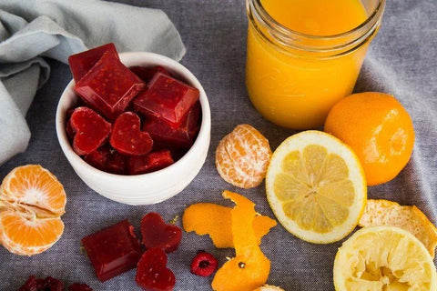 orange and Raspberry Gummies in a bowl surrounded by orange juice, oranges, raspberries and orange peel
