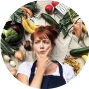 Jen Thomson laying down surrounded by fruits and vegetables with a thinking impression on her face