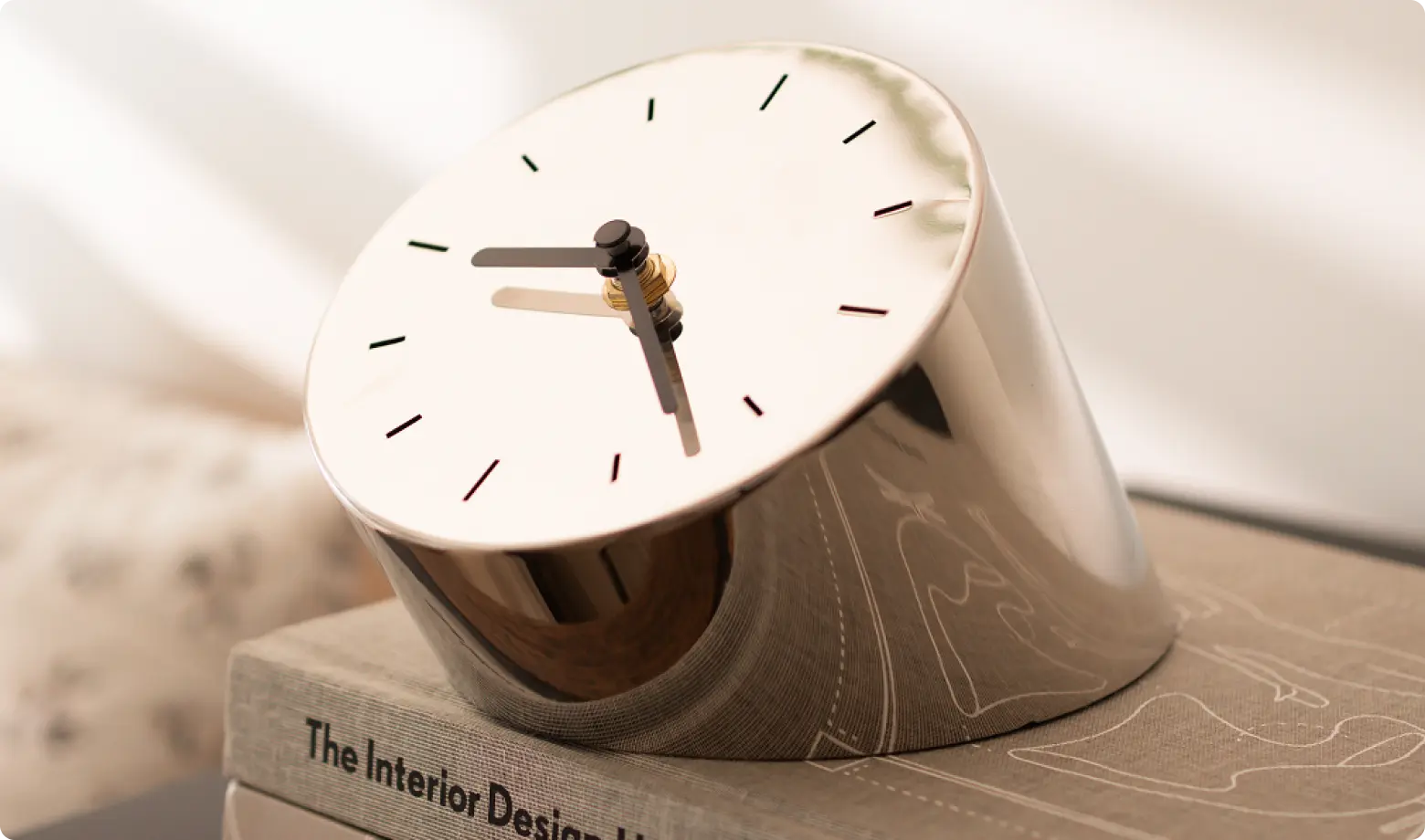 Modern metallic desk clock with tilted design, placed on an interior design book.