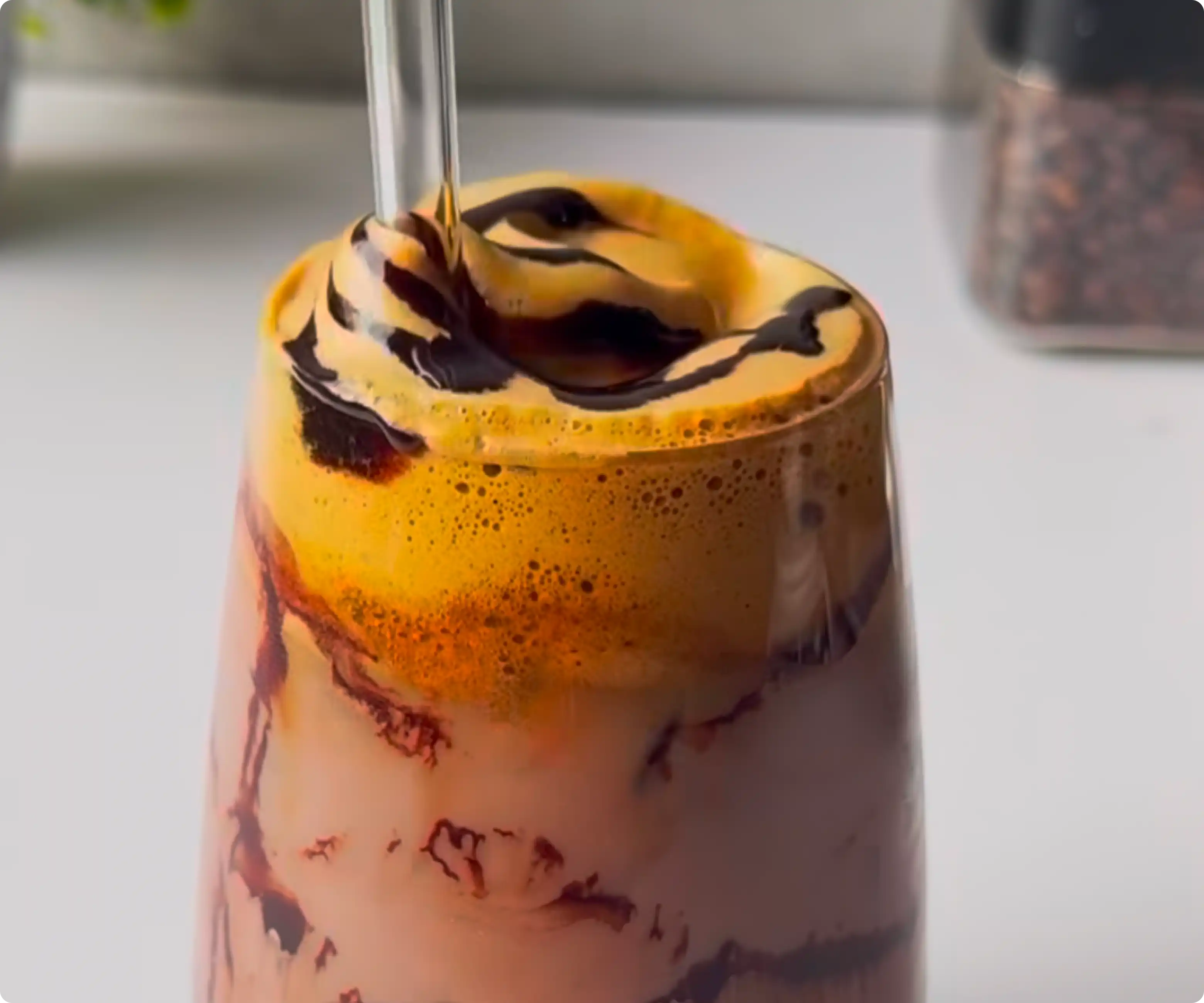 Iced chocolate dalgona coffee with whipped coffee foam and mocha drizzle in a clear glass