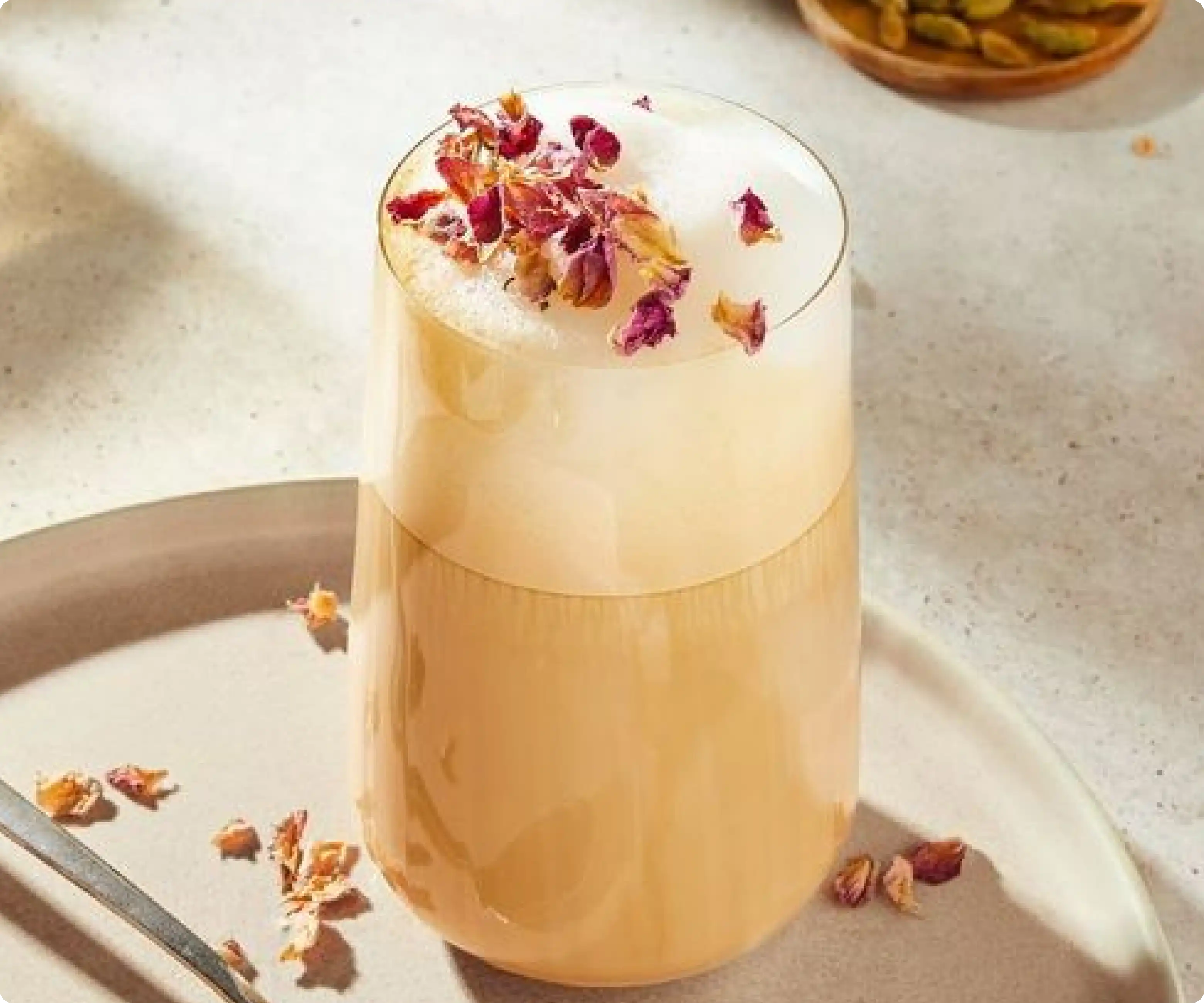 Rose cardamom iced coffee with milk, garnished with a rose petal and served in a glass cup
