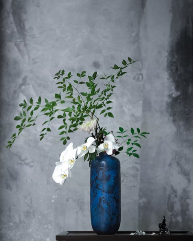 A dark blue vase filled with a mixture of wildflowers in various colors and sizes spilling out over the edges.
