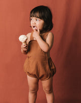 Baby eating an ice cream cone wearing the Noble Sun Suit in Cinnamon color