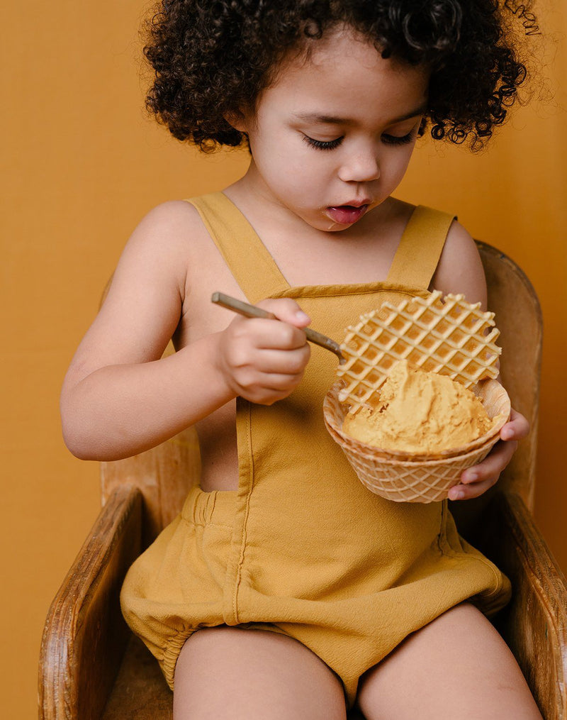 Baby eating ice cream out of a waffle bowl wearing the Noble Sun Suit in Turmeric color