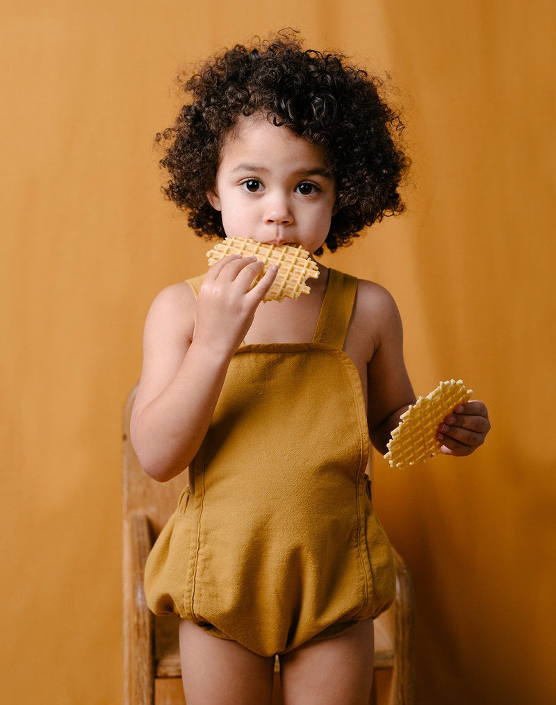Baby eating waffle wafers wearing the Noble Sun Suit in Turmeric color