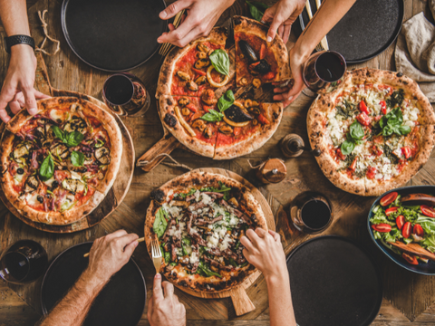 Four pizzas on a table with glasses of red wine