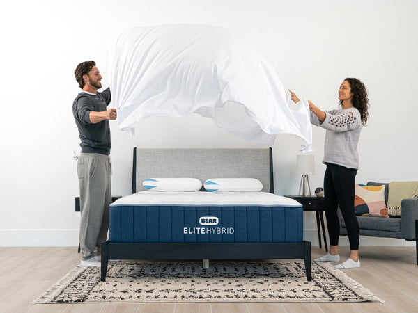 Two people lifting up a mattress sheet