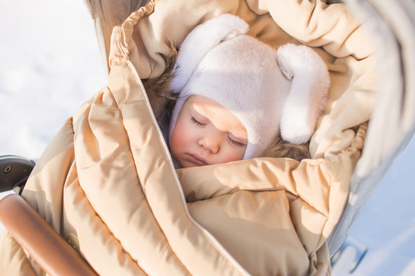 A baby wrapped up sleeping in a stroller outside.