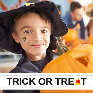 Boy with smiling jack-o-lantern temporary tattoo on his cheek holding a pumpkin.