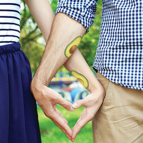 Forming a heart with their hands, a couple wears matching avocado tattoos for Valentine's Day.