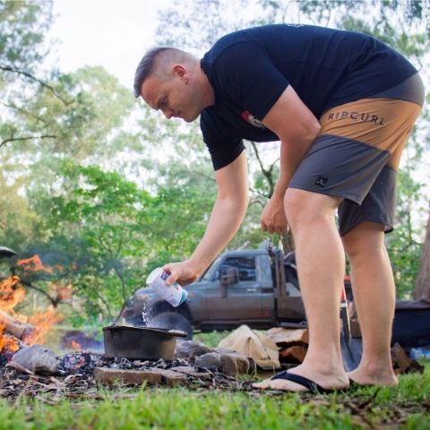 Man making ginger beer damper over in pot over campfire