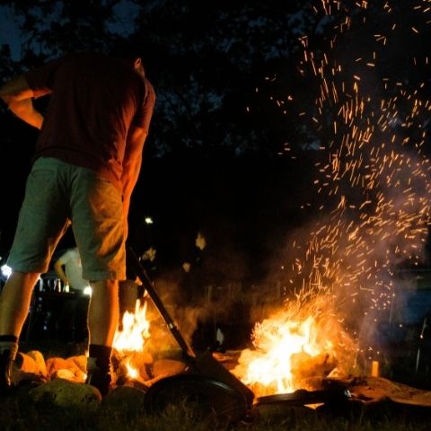 Man stoking a campfire with a shovel at night