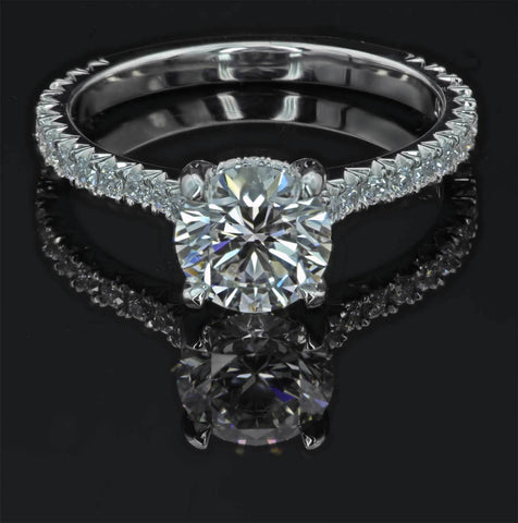 Diamond engagement ring against back background. Round center diamond with fishatil round stones going down the side of the shank. All white diamonds