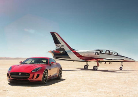 A red F-Type Jaguar car next to a private plane in the desert