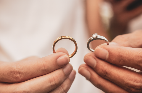 Two ring being held in hands. One is an engagement ring, the other is a wedding band