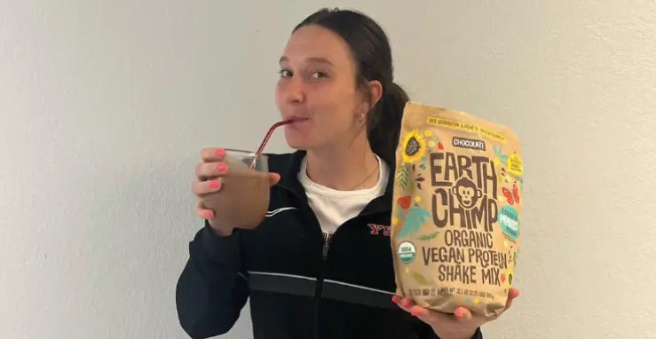 Woman drinking a shake, holding Earthchimp vegan protein powder mix, hinting at meal replacement use.