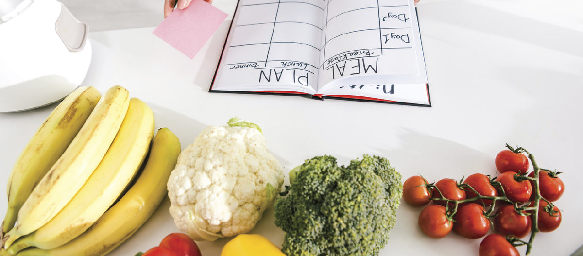 A meal planner with fruits and vegetables on the side