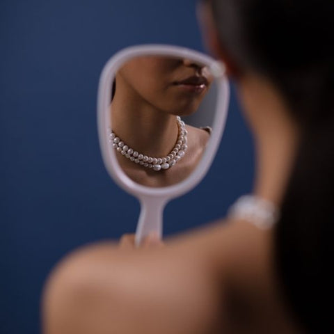 Frau mit Süßwasserperle um den Hals betrachtet sich im Spiegel
