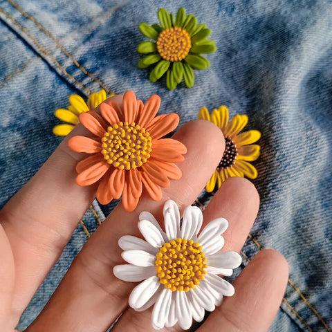 little daisy brooch of different colors and a hand showing 2 of them