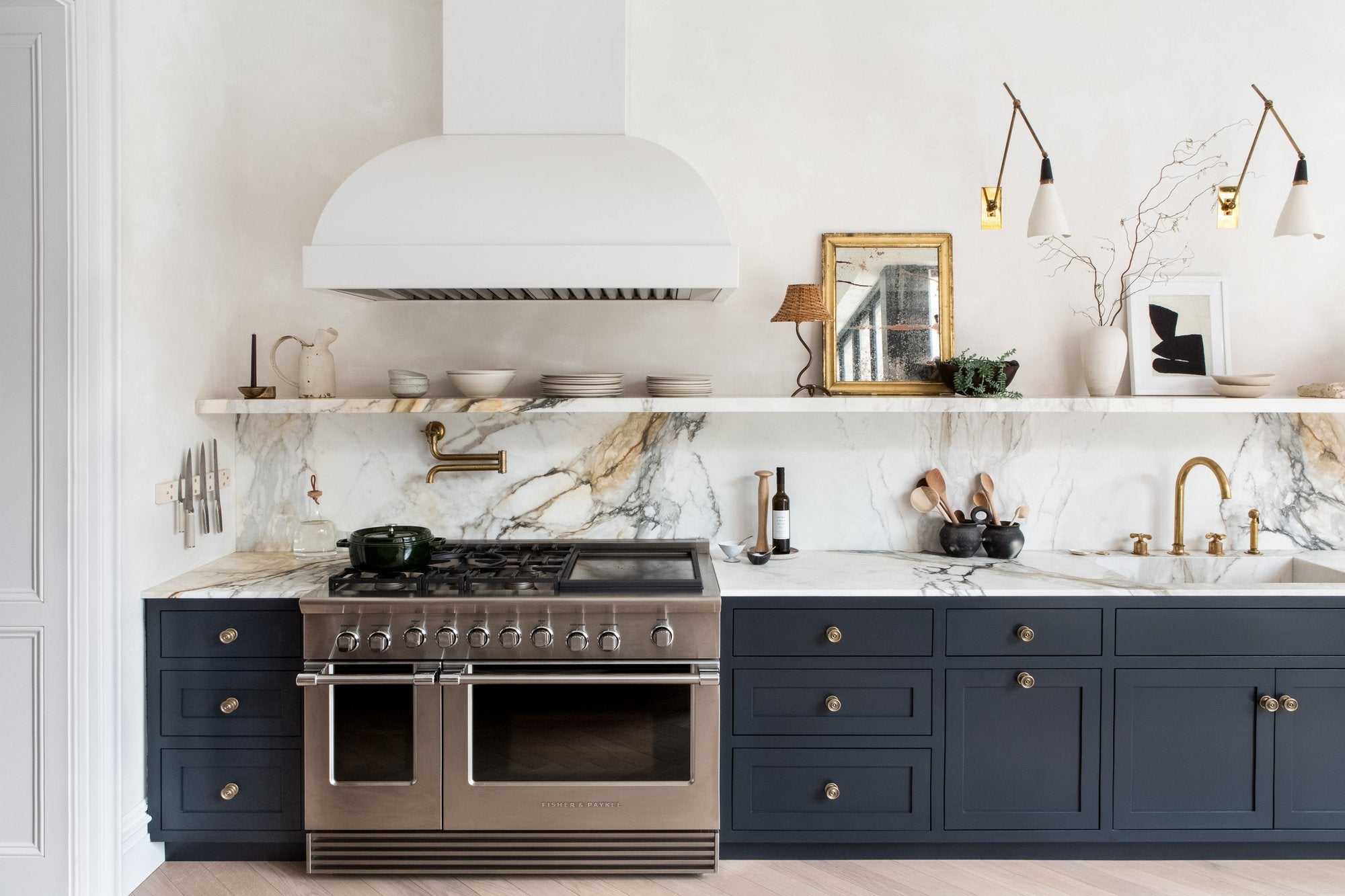 Brass kitchen hood, marble slab backsplash, navy blue kitchen cabinets