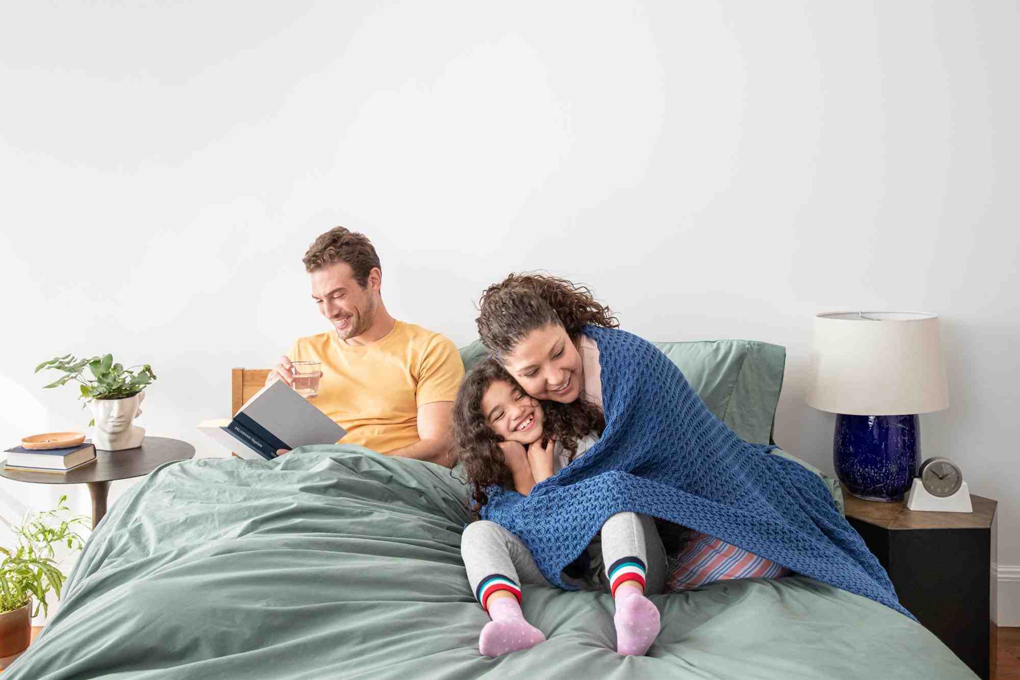 Family of three sitting on their Tuft & Needle bed smiling and laughing