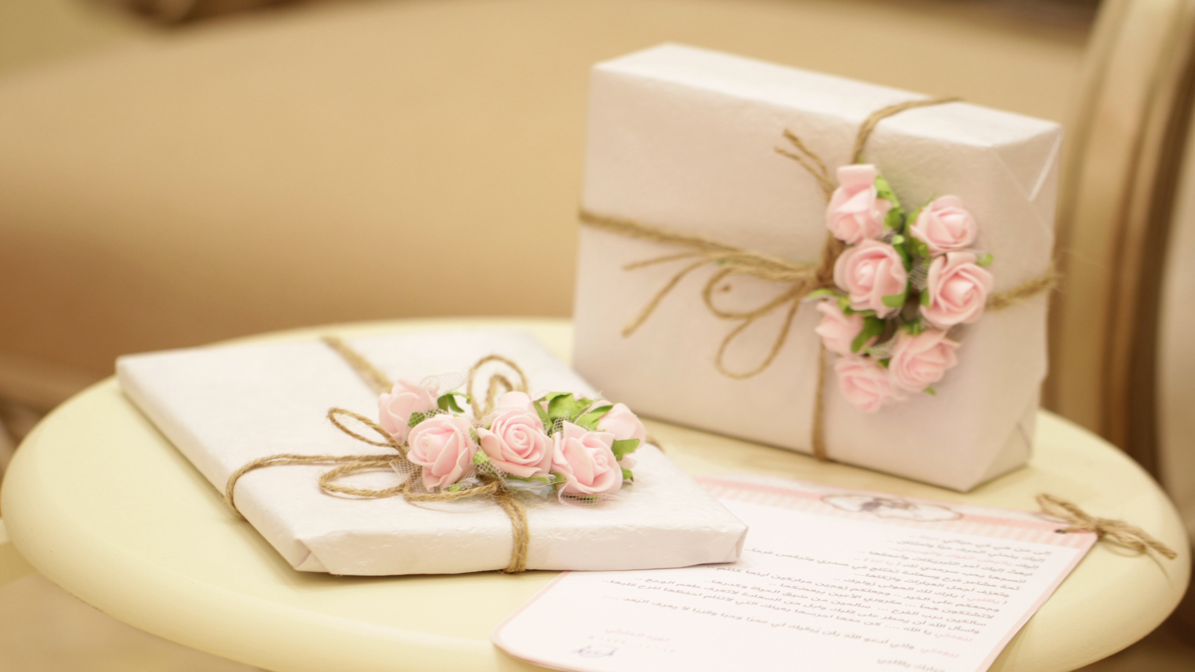 Two presents wrapped in white with pink roses attached to them