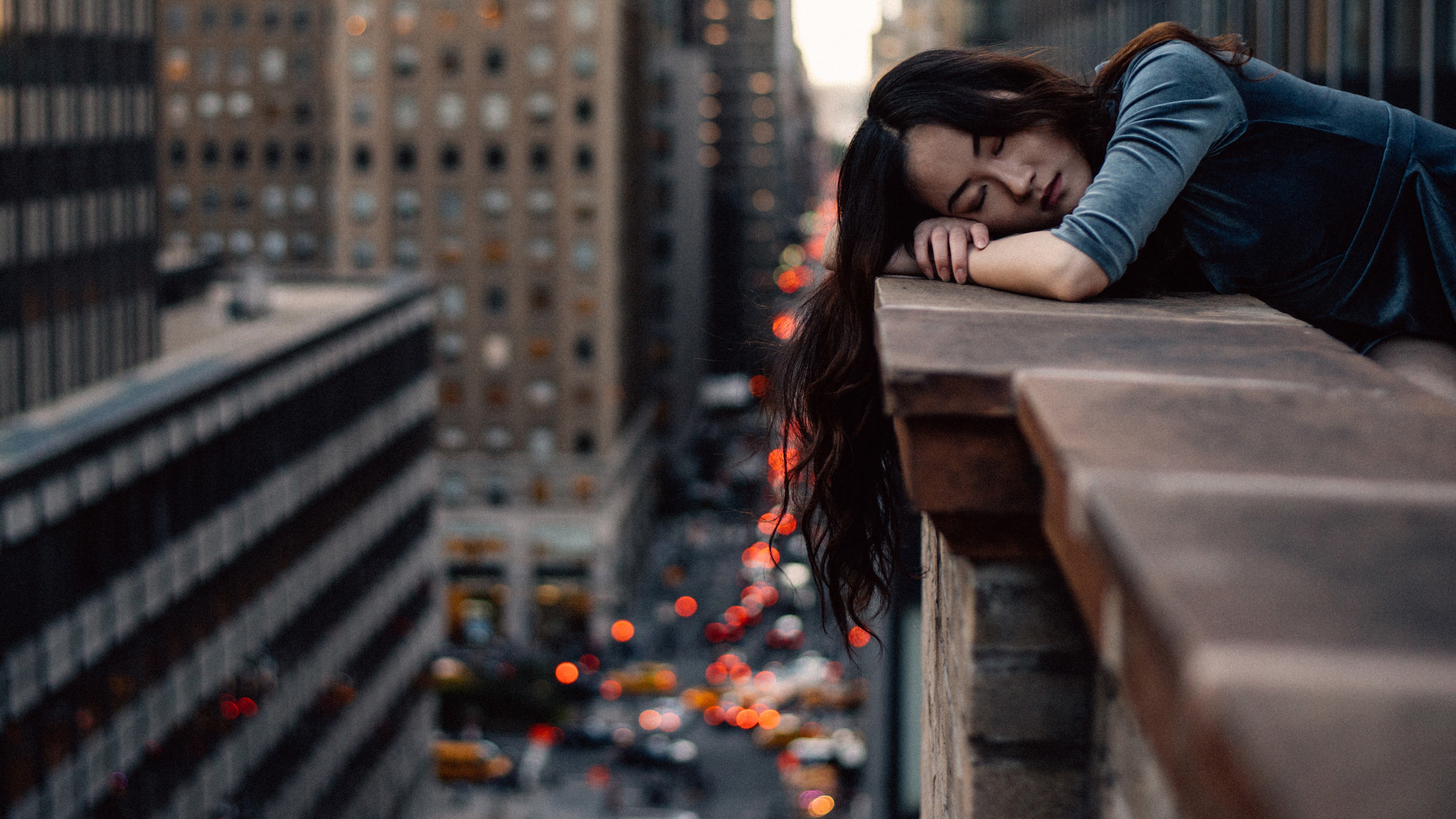 Woman leaning her head on the edge of a tall building in a busy city with her eyes closed, depicting someone with Narcolepsy