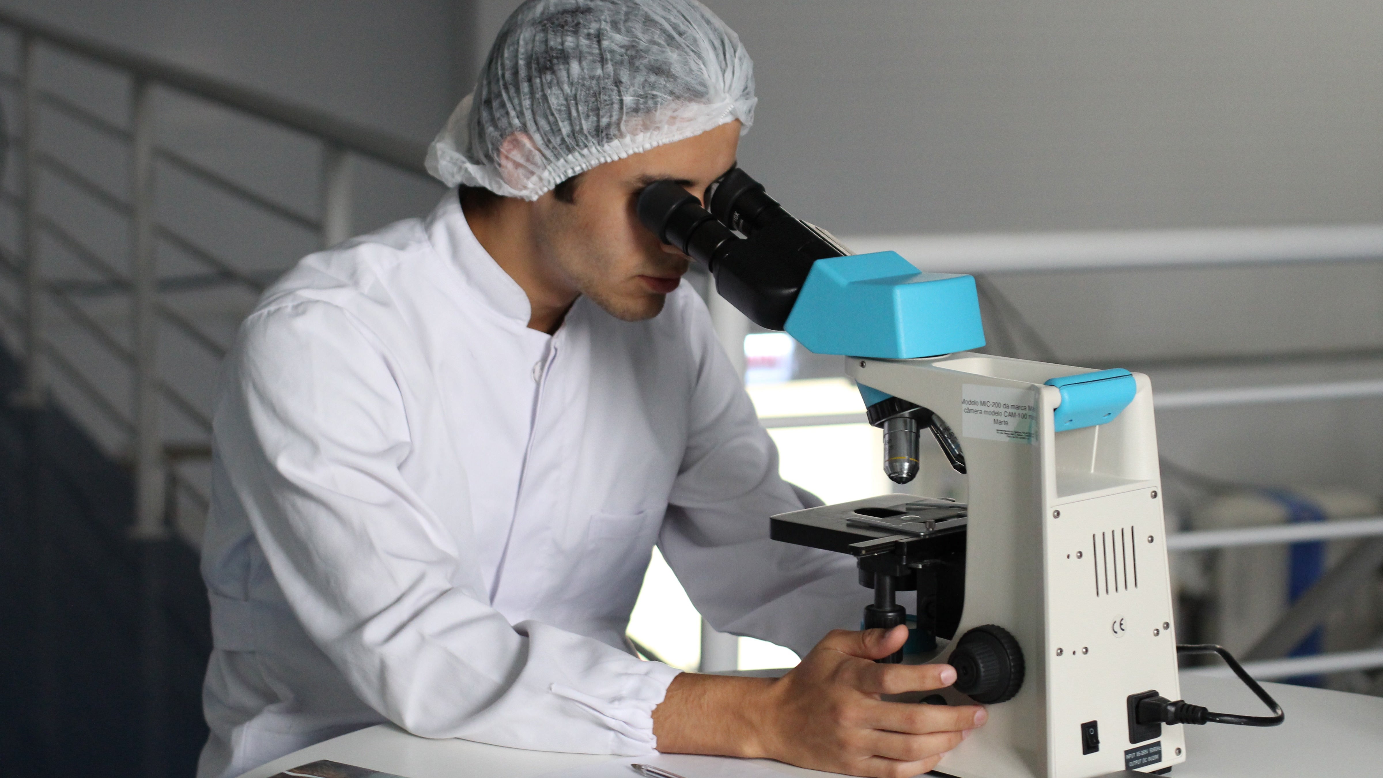 Scientist looking thru a microscope with a hair net on