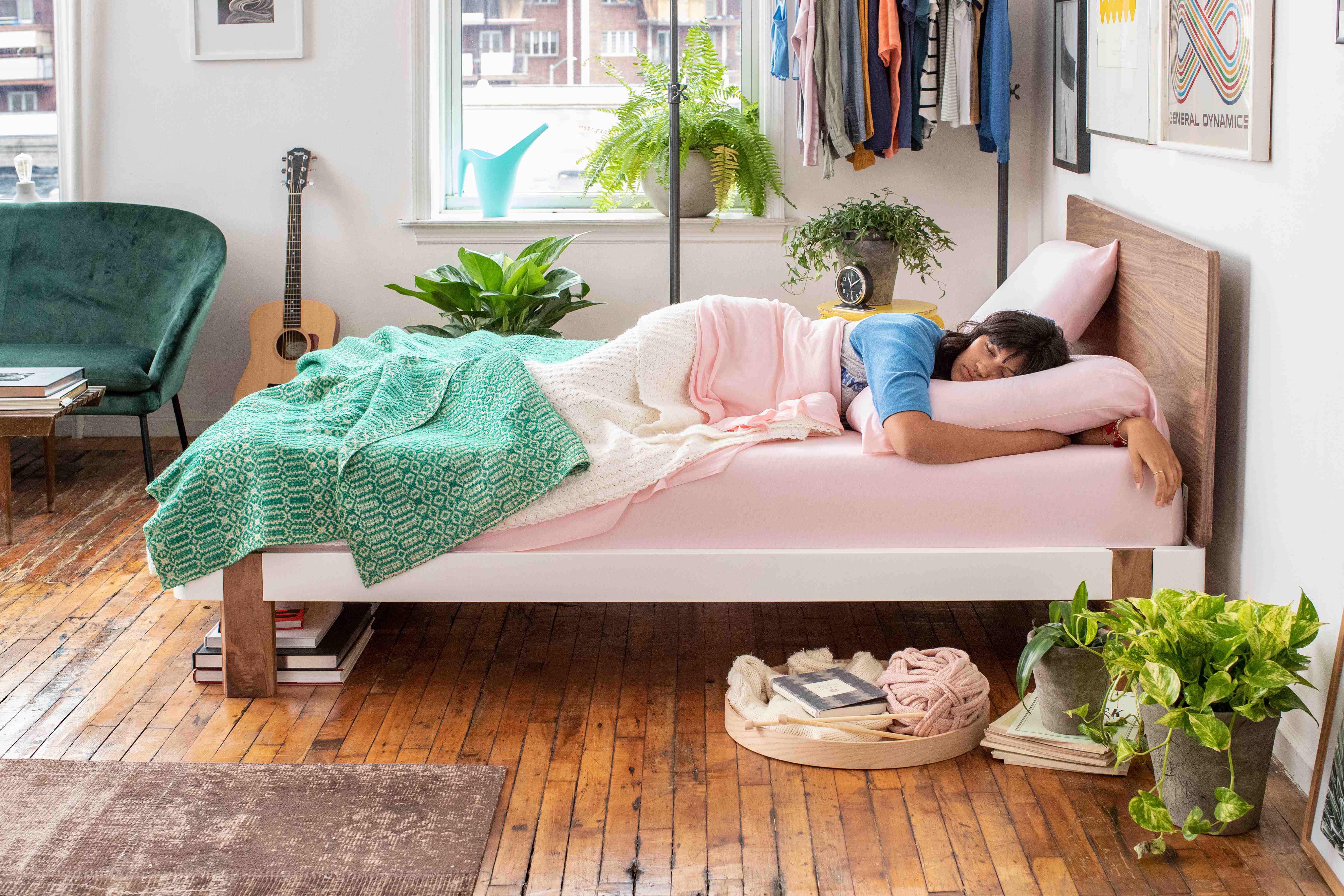 Woman sleeping on a Tuft & Needle Original mattress on her side in her bedroom with plants, clothes and a guitar
