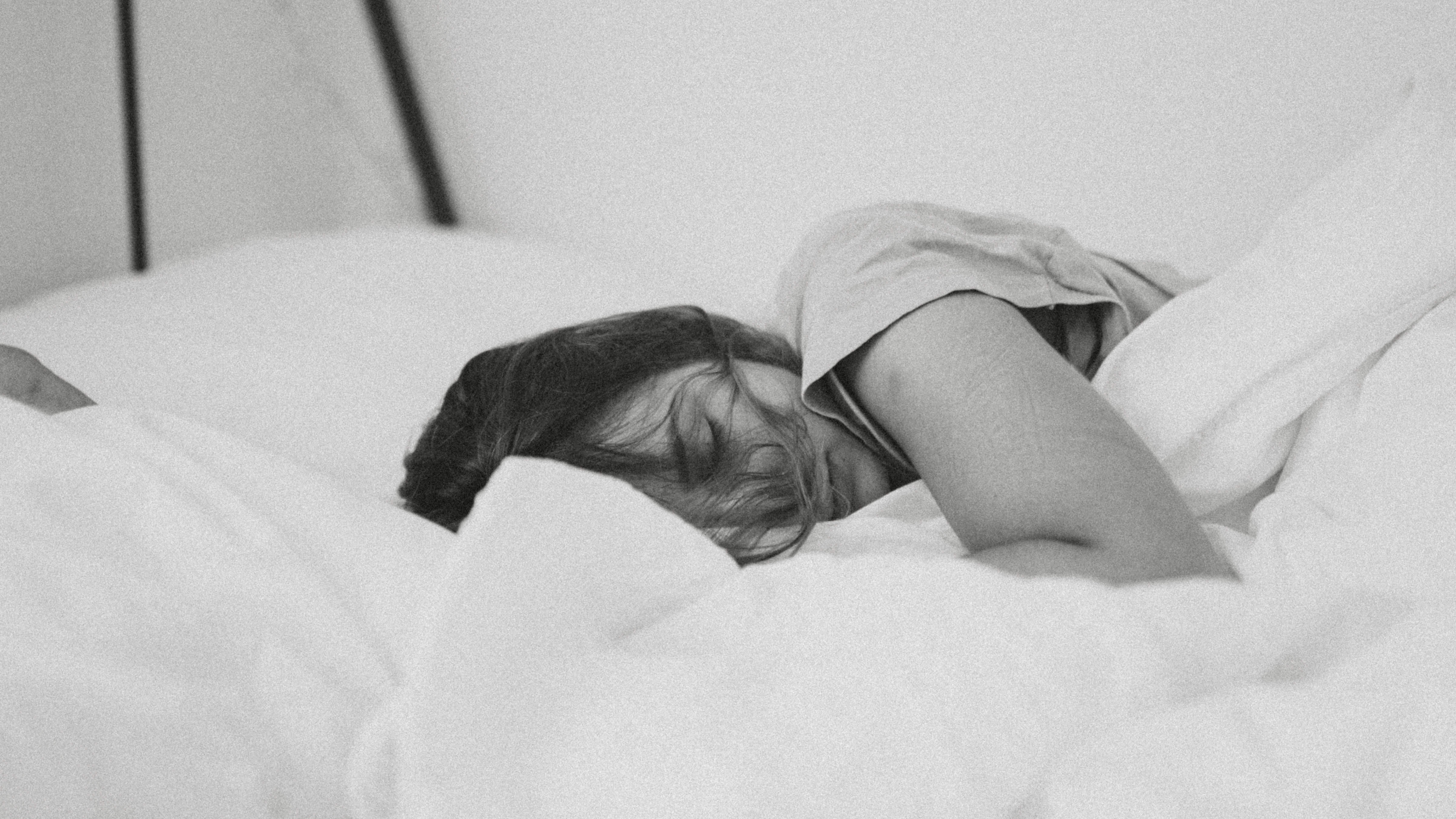 Woman sleeping in white bedding on her side with hair over her face. The picture is in black and white.