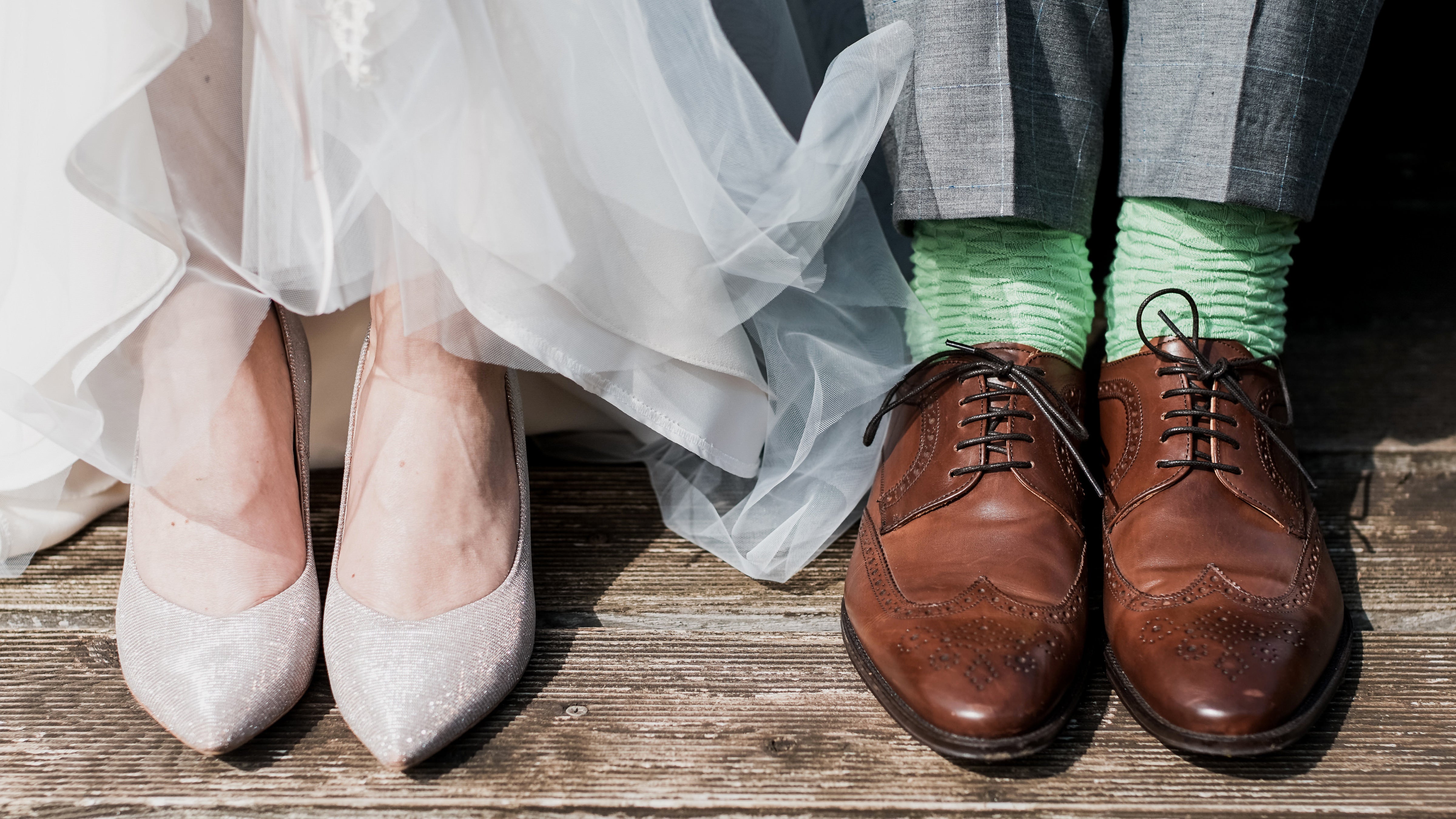 Woman sparkly wedding shoes next to mens brown dress shoes on a wood floor