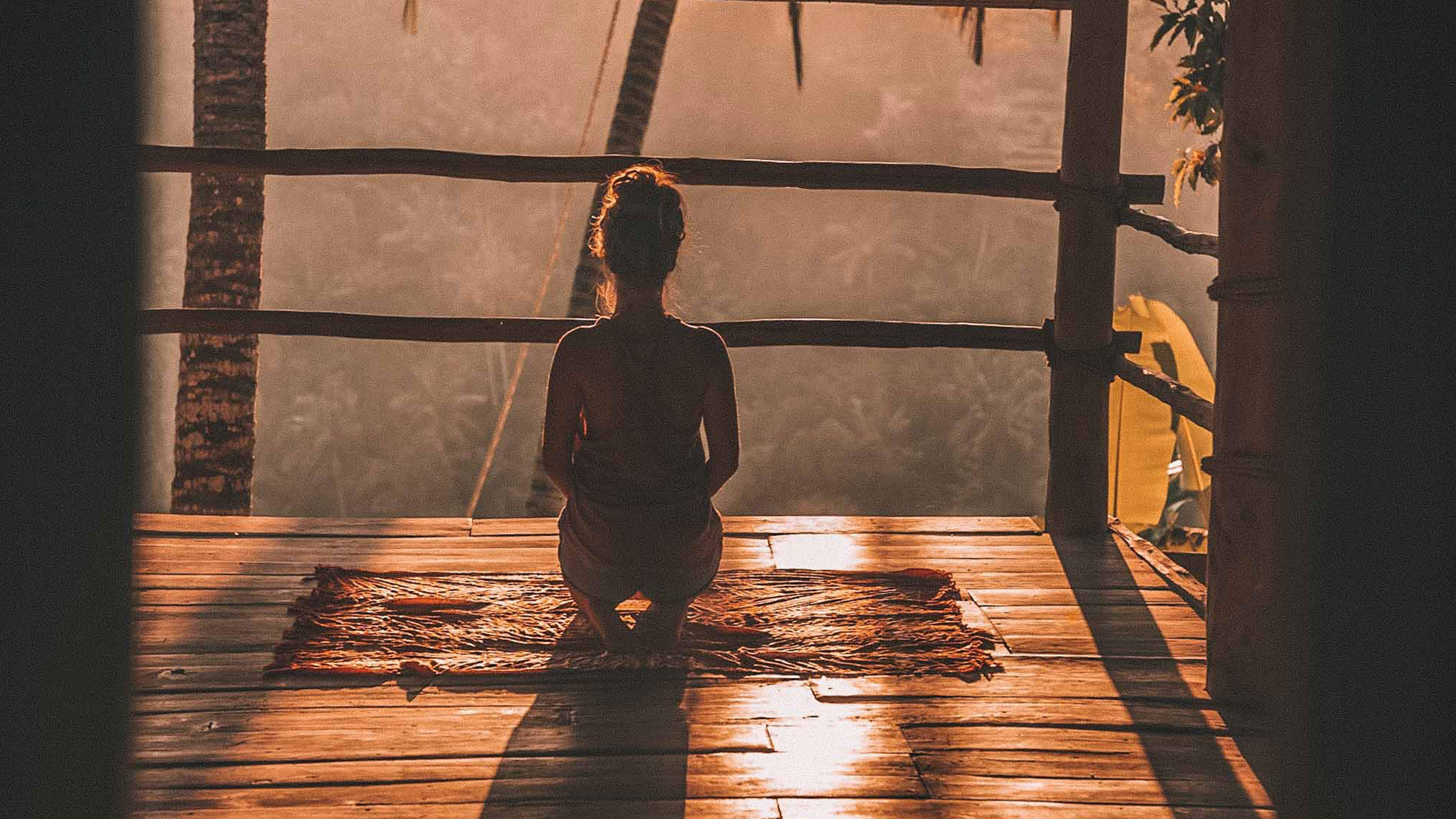 Woman kneeling and meditating on a rug overlooking a jungle