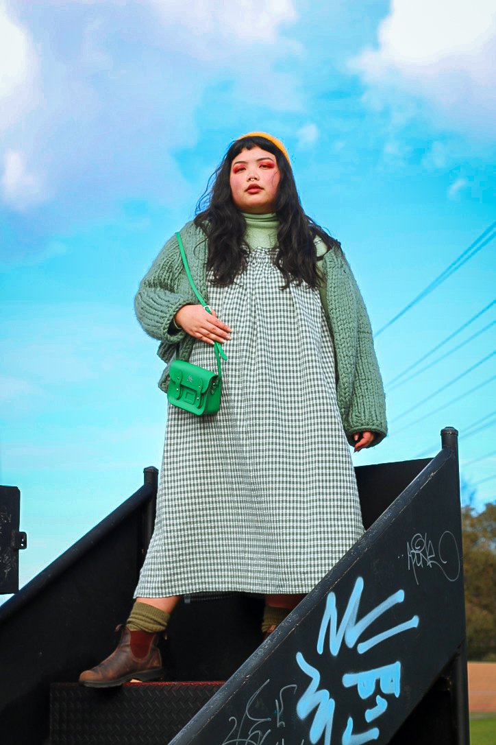 Nadia wears: Sister gingham dress, Uniqlo skivvy, Handmade knit cardigan, Stussy yellow beanie, Cambridge Satchel Co. green crossbody bag, Models own socks and Blundstone boots. Photo by Hayley Hughes