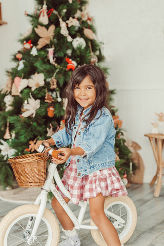 little girl riding banwood balance bike in front of christmas tree