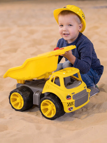 boy sitting in sandpit with dumper truck