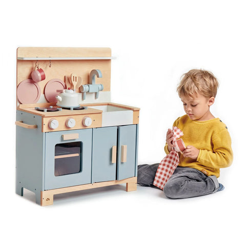 boy sitting next to classic world wooden role play kitchen