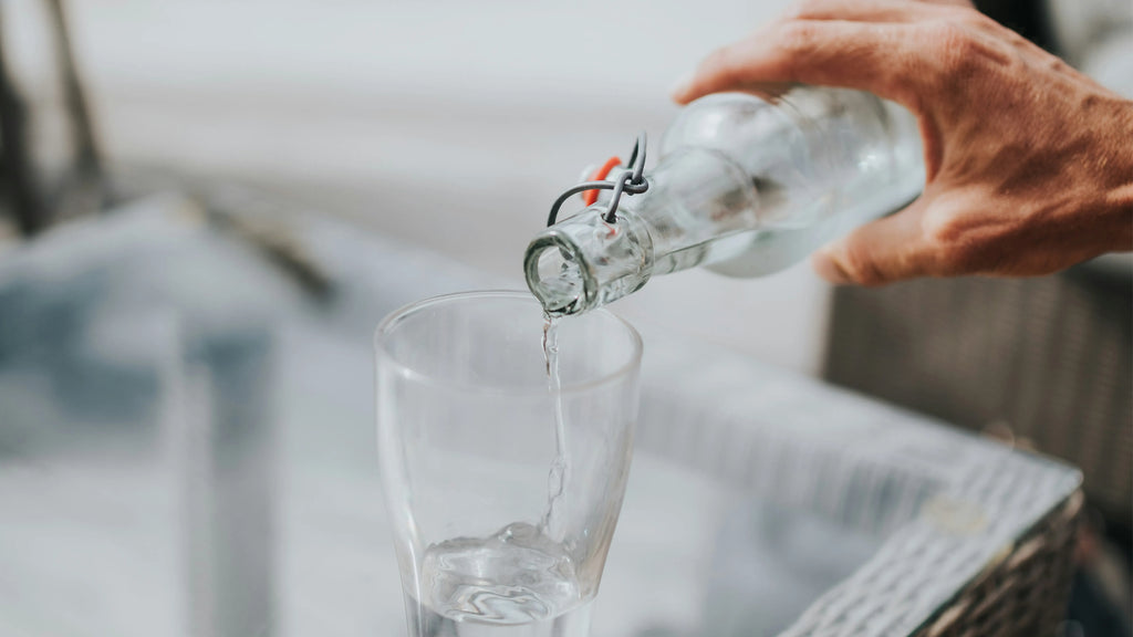 Hand pouring water from glass bottle into drinking glass