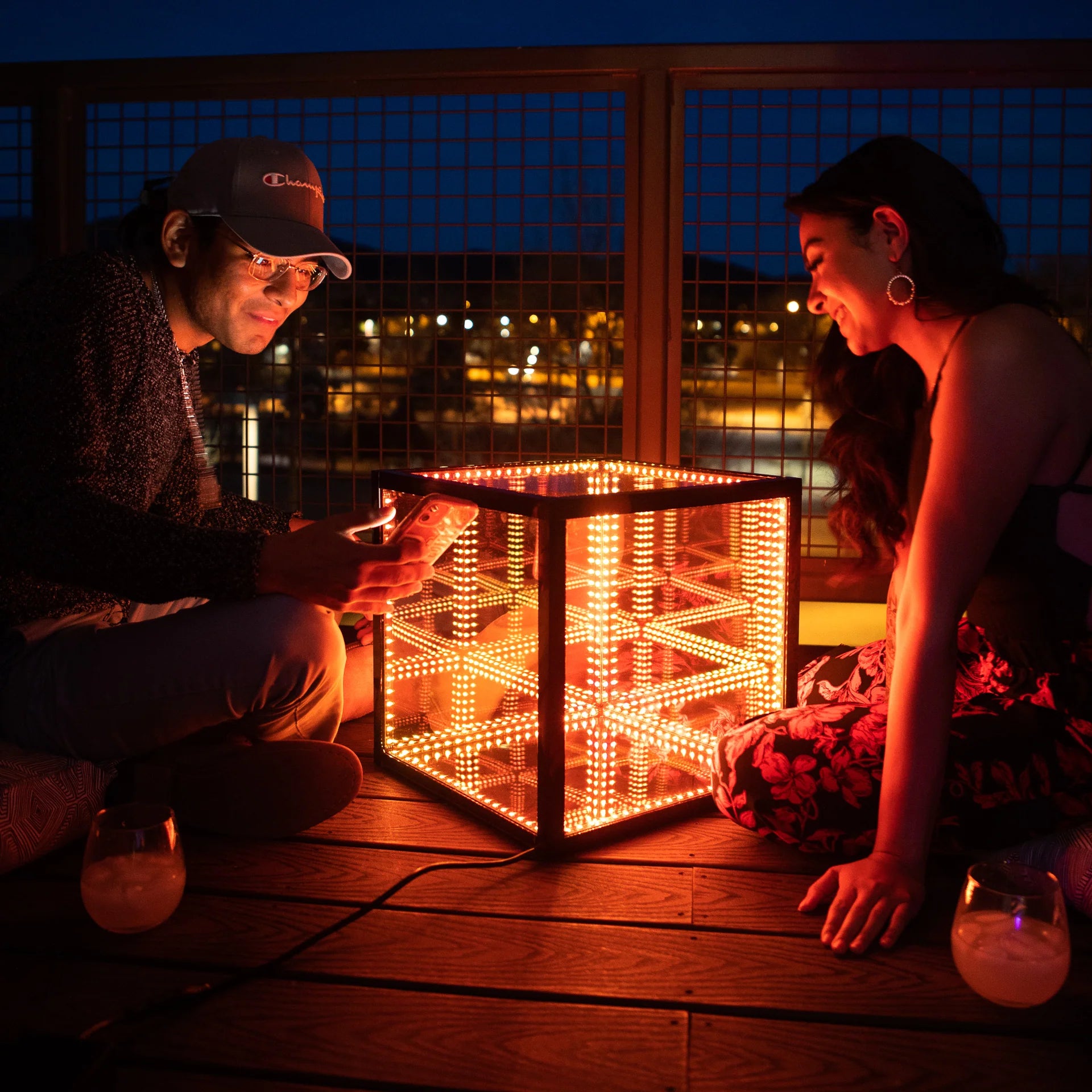 A woman and a man sitting on a wooden deck illuminated by colorful Halloween lights
