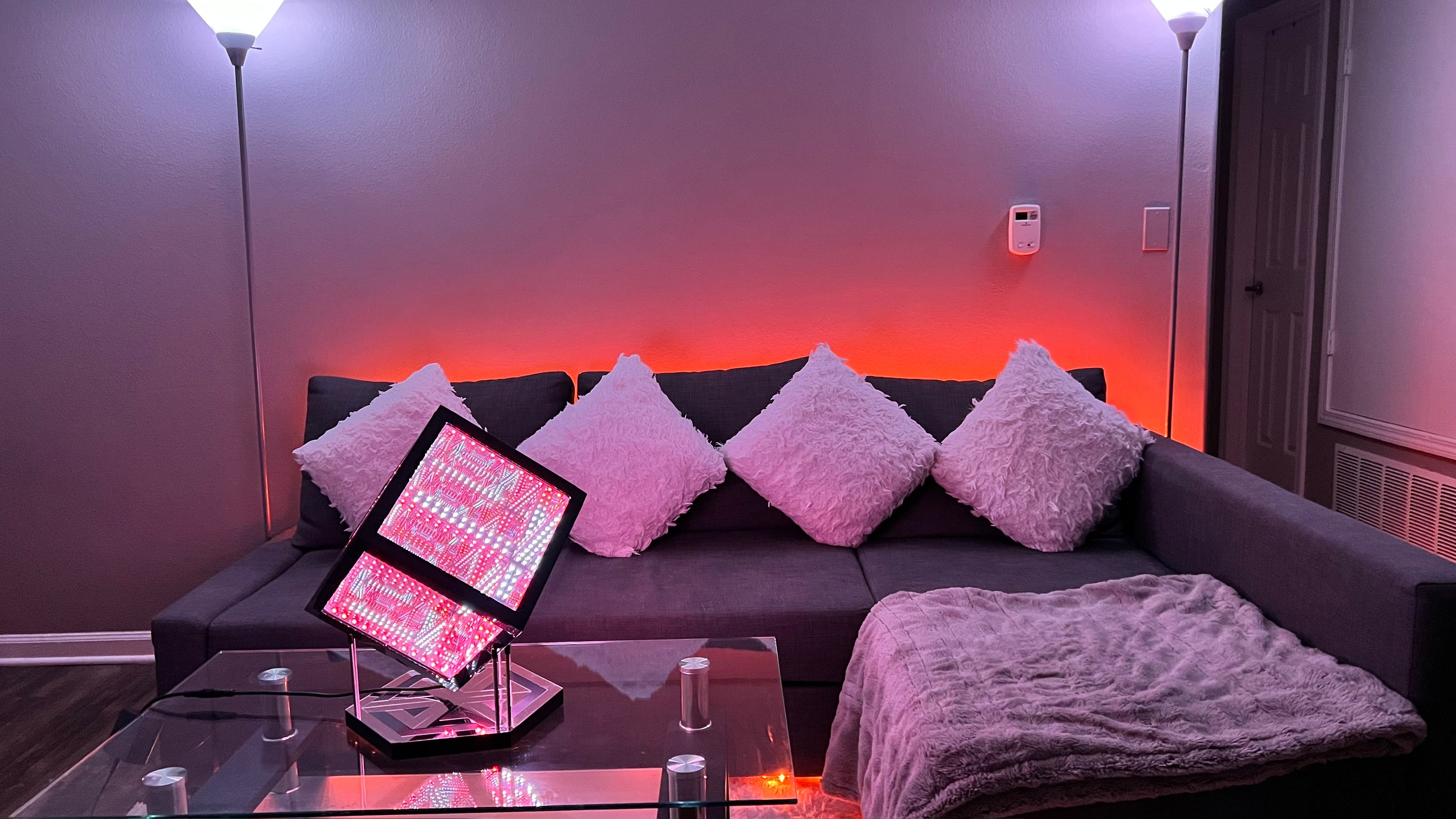 Living room, with a couch and four pillows on it illuminated by backlighting from LED color changing lights, and a Hypercube on the coffee table