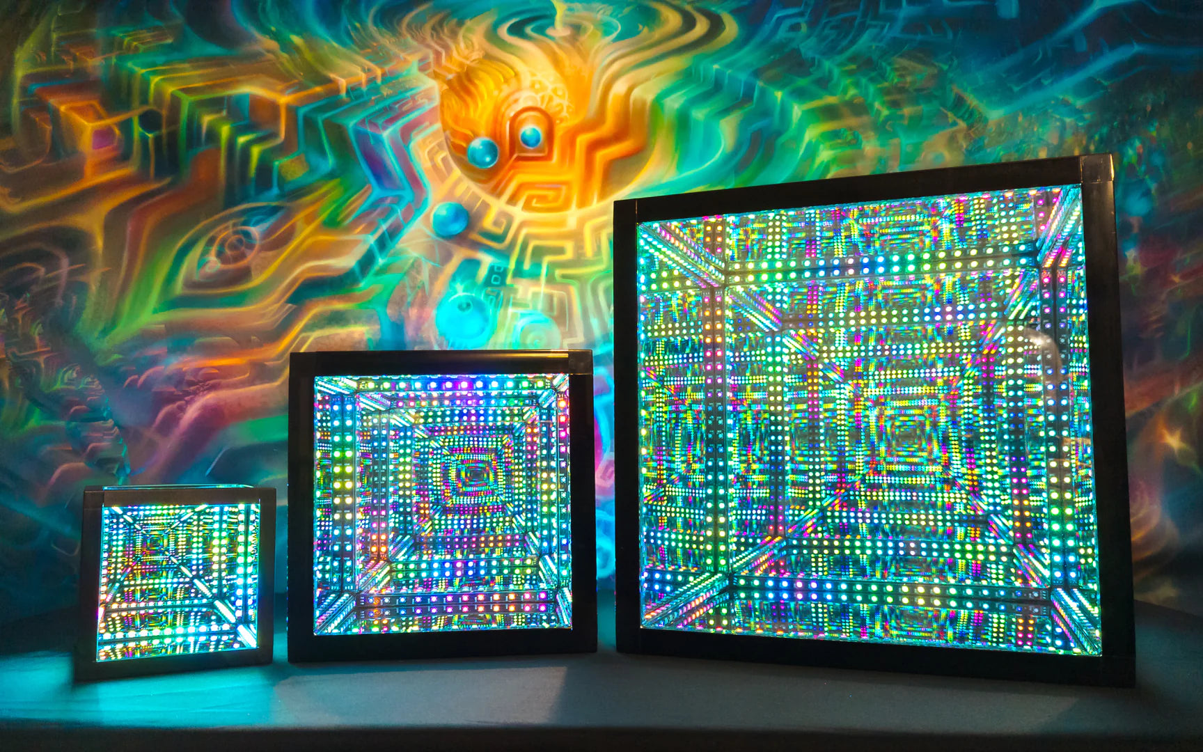 Three psychedelic art pieces in front of a colorful wall illuminated by the best Christmas lights.