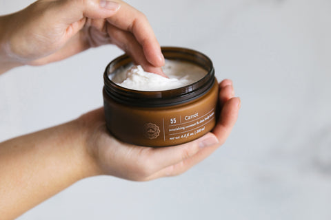 A hand holding a jar of Saje carrot body butter in their palm