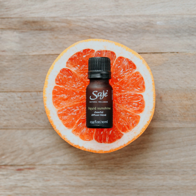 Liquid sunshine diffuser blend on a pink grapefruit slice on top of a wooden background