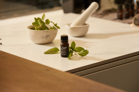 A Saje essential oil diffuser blend on a counter with sprigs of mint around it