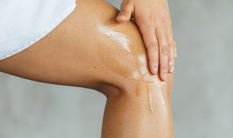A person applying a Saje body oil to their leg
